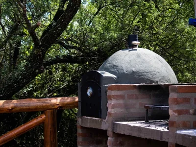 Horno a leña rústico y parrilla en posada de Nono, rodeado de árboles.